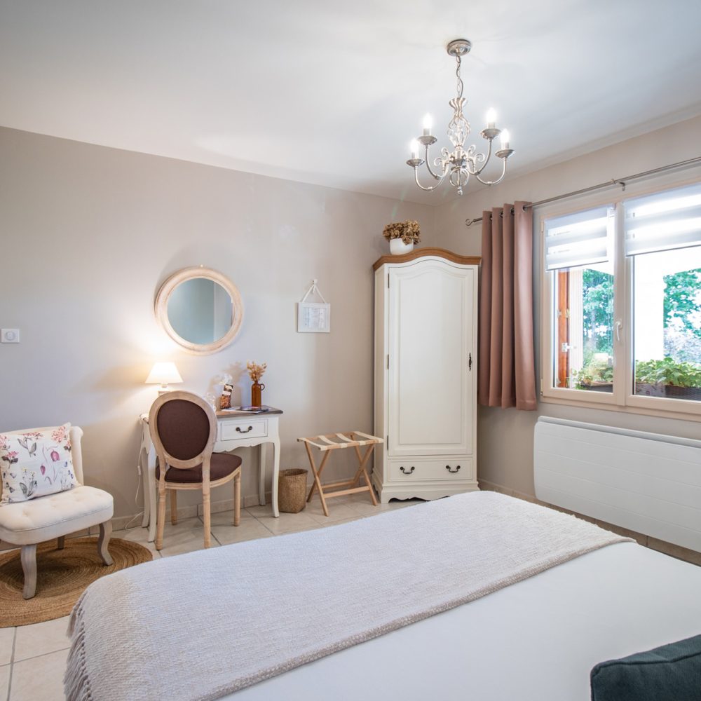 Lit double de la Chambre Bergerac près d'une fenêtre habillée de rideaux