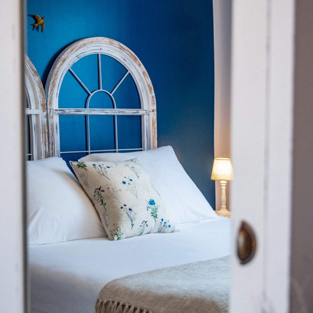 Tête de lit bleue, coussin brodé et lampe de chevet dans la Chambre Brantôme