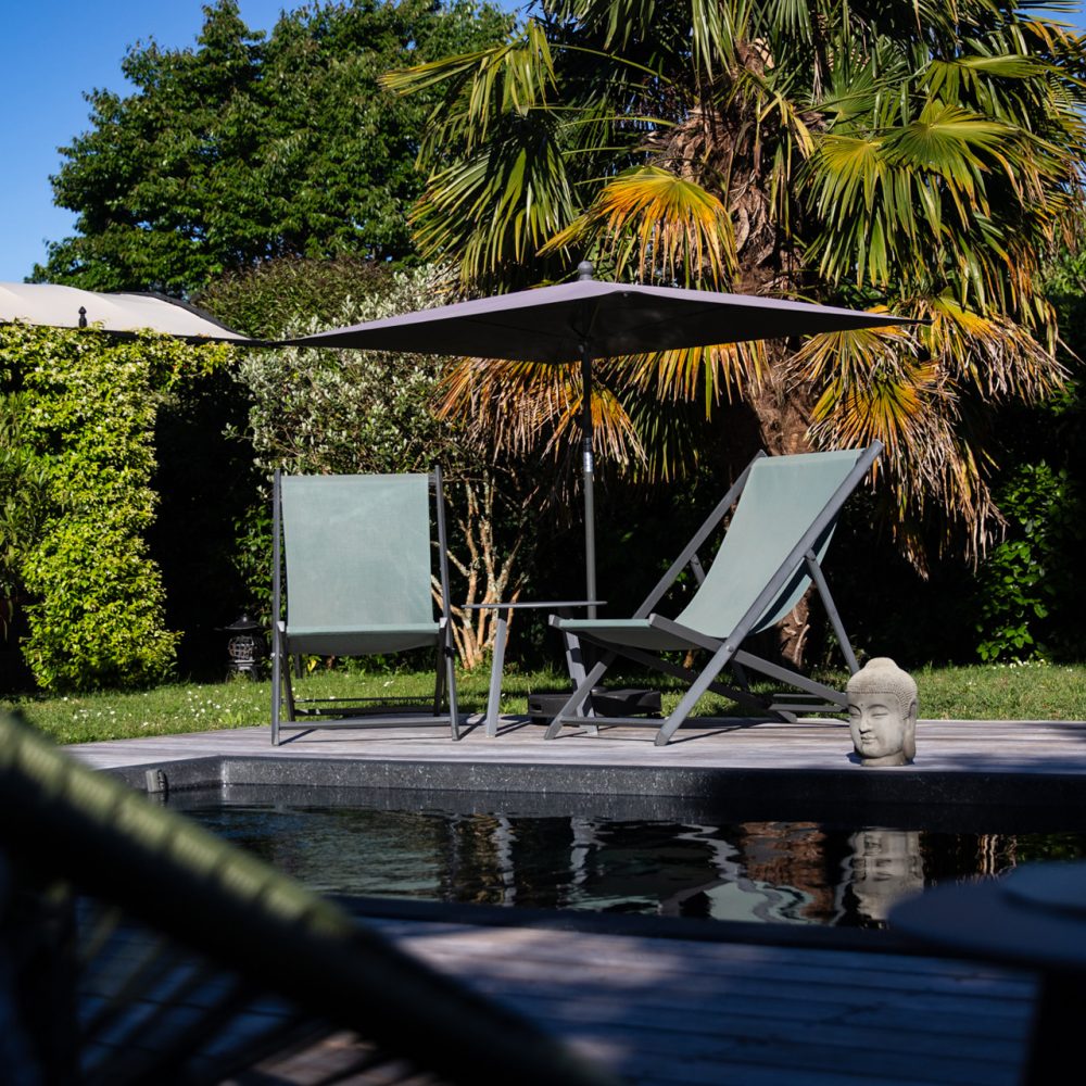 Piscine et transats sous parasol entourés de verdure, chambres d’hôtes avec piscine à Sarlat