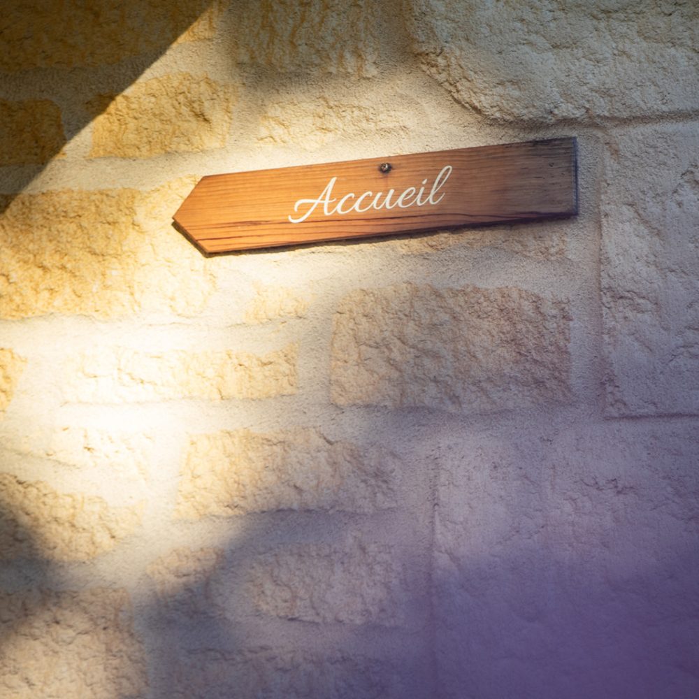 Panneau « Accueil » en bois éclairé sur un mur en pierre, chambres d’hôtes à Sarlat