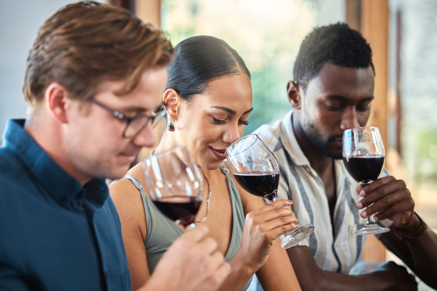 Diversity, luxury and friends wine tasting at a restaurant or vineyard, smelling alcohol in a glass together. Young carefree people bonding and having fun, enjoying a wine tour at a distillery.