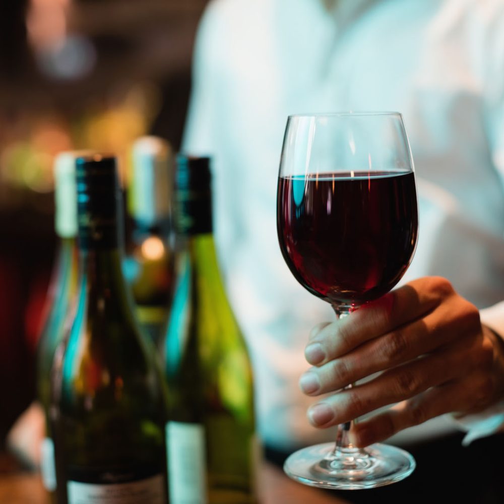 Mid section of bartender holding glass of red wine at bar counter